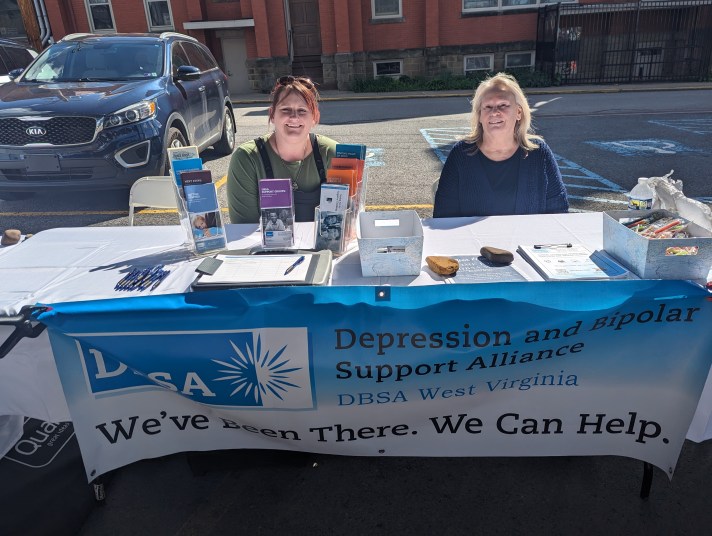 DBSA WV staff sitting behind table with banner, pamphlets, flyers, and pens.