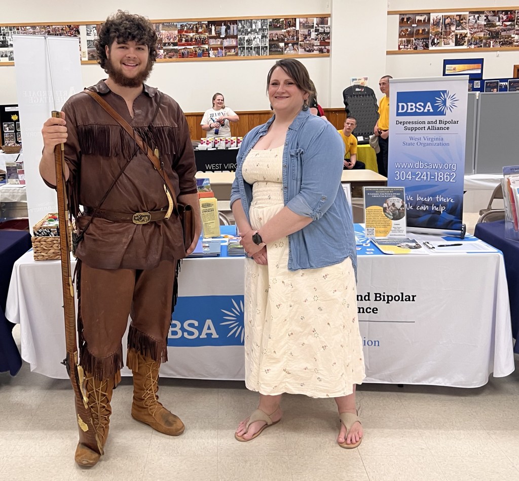 The Mountaineer, WVU's mascot, and Stacie Weaver stand in front of the DBSA WV table