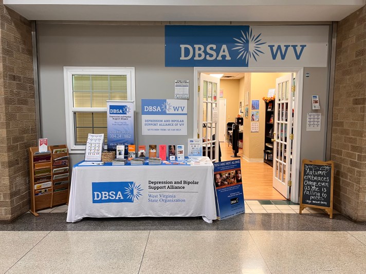 DBSA WV exhibitor table. Signs, flyers, brochures, and stickers are on the table. Table cloth reads "Depression and Bipolar Support Alliance West Virginia State Organization"