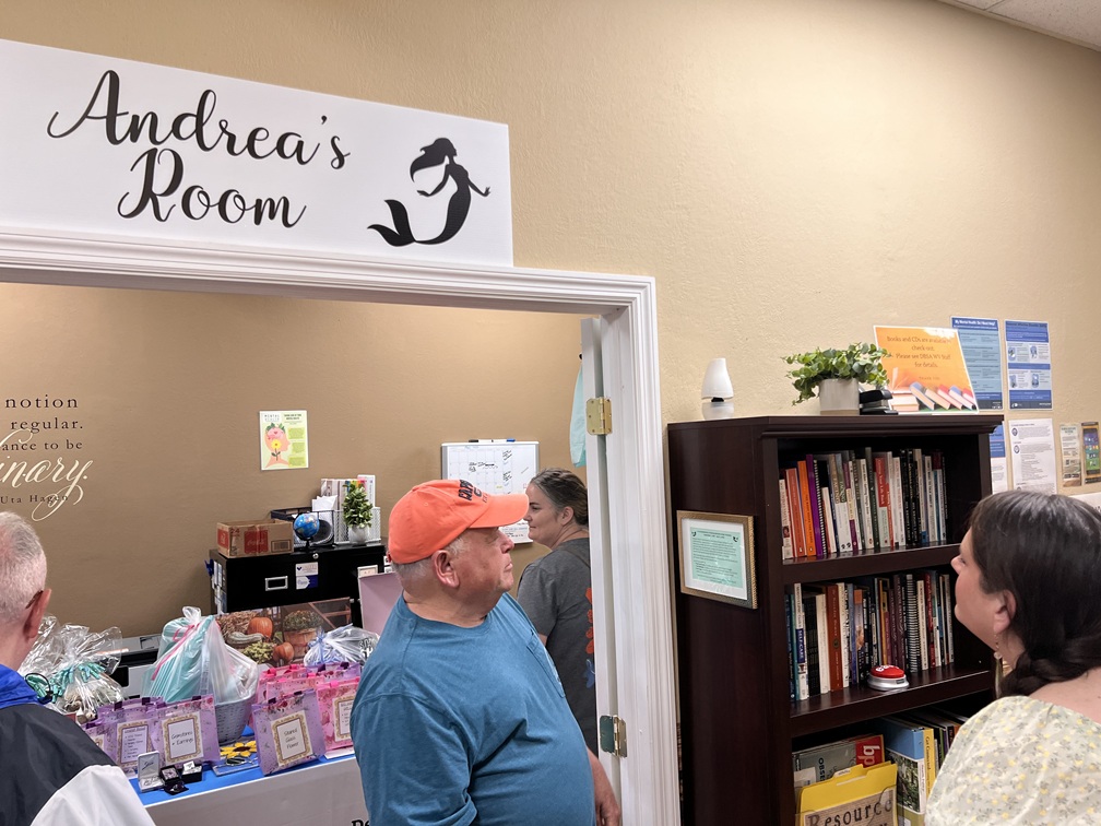 People looking at a framed plaque outside a doorway with a sign that reads "Andrea's Room".