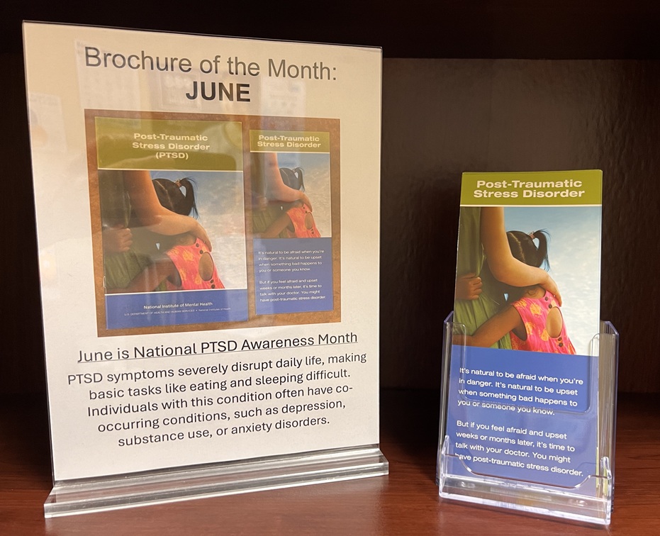 A stack of brochures beside a sign that says Brochure of the Month: June. June is National PTSD Awareness Month. PTSD symptoms severely disrupt daily life, making basic tasks like eating and sleeping difficult. Individuals with this condition often have co-occurring conditions, such as depression, substance use, or anxiety disorders.